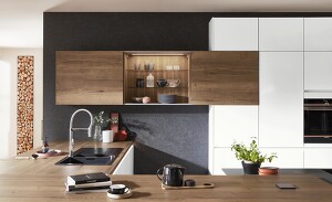 Perfektes Zusammenspiel von Farben und Licht. Die matte alpinweiße Küche und die dunkle Wand fassen Arbeitsplatte und Schränke aus Holzoptik optimal ein. Tolles Extra: Wandschrank mit Schiebetüren, der durch seine Innenbeleuchtung mehr Behaglichkeit bringt.  Perfektes Zusammenspiel von Farben und Licht. Die matte alpinweiße Küche und die dunkle Wand fassen Arbeitsplatte und Schränke aus Holzoptik optimal ein. Tolles Extra: Wandschrank mit Schiebetüren, der durch seine Innenbeleuchtung mehr Behaglichkeit bringt.
