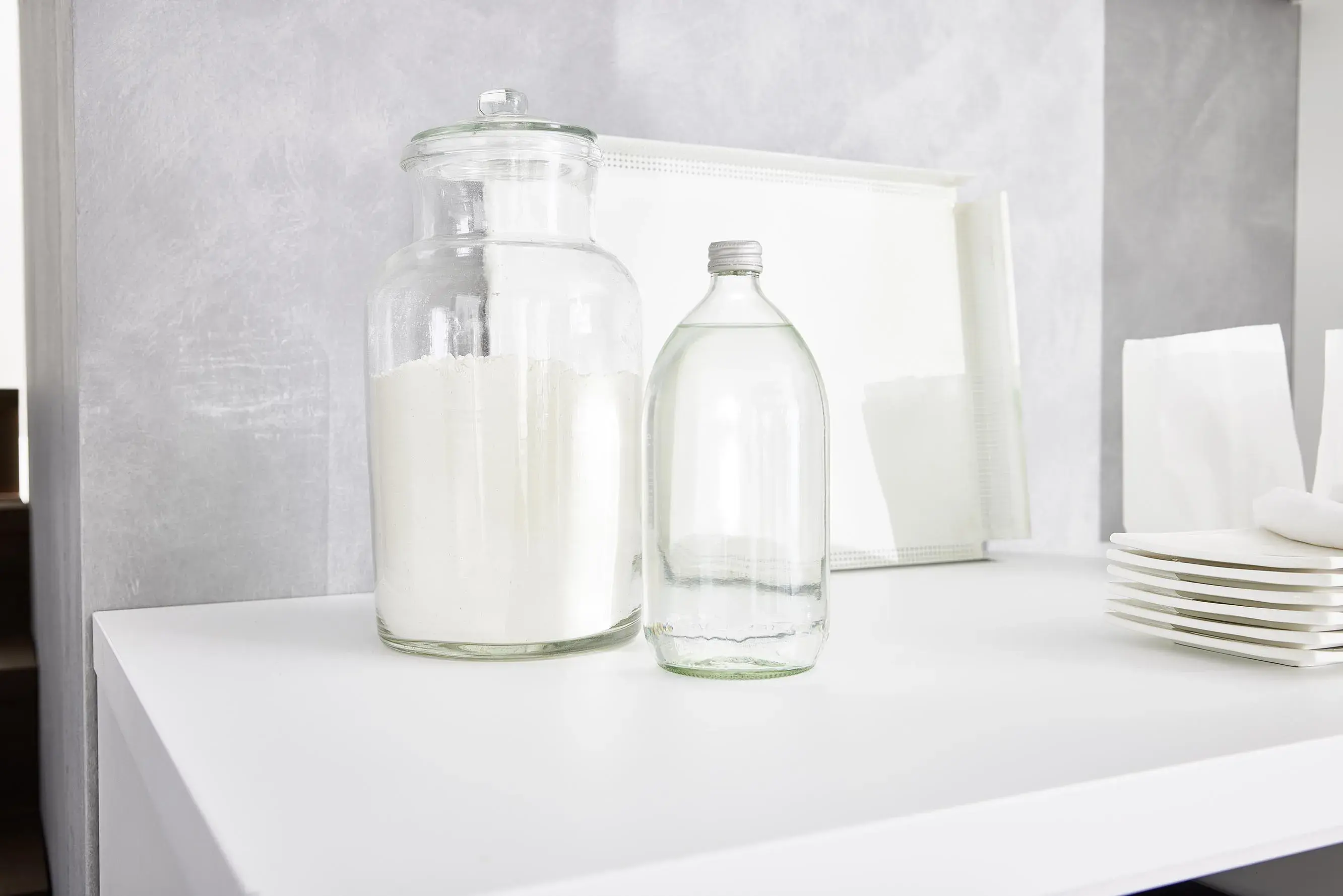 NOBILIA Alpinweiß Moodshot - Aufbewahrungsbehälter aus Glas mit Mehl und Wasserflasche neben Tellerstapel, Detailansicht